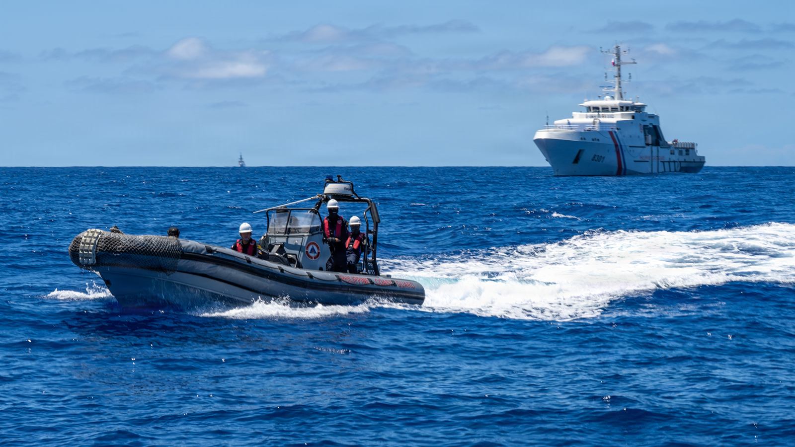 Philippine Coast Guard personnel driving a rigid-hull boat during a search and rescue drill, with BRP Gabriela Silang behind them.